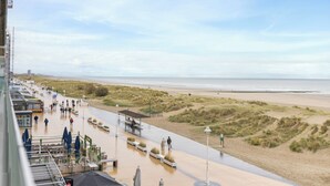 Un paseo marítimo a orillas de una playa arenosa, con un muelle y zonas de estar, y vistas al mar.