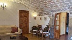 Un saló d'estar acollidor amb sostre de maó, una porta de fusta, un sofà, dues butaques i una taula petita.