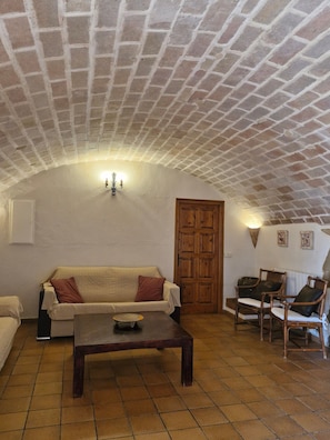 A cozy living room with a brick ceiling, a wooden door, a beige sofa, two wicker chairs, and a coffee table. - La Parra at Mas Pareta: Rural Retreat Surrounded by Nature (Fonolleres (Parlavà))
