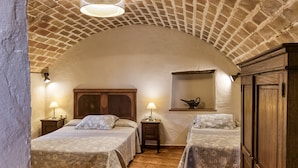 Een kamer met twee bedden, een houten hoofdeinde, een klein plankje met een lamp en een bakstenen plafond.