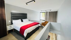 Un dormitorio moderno con una cama grande, una mesita de noche, una silla y una ventana con cortinas.