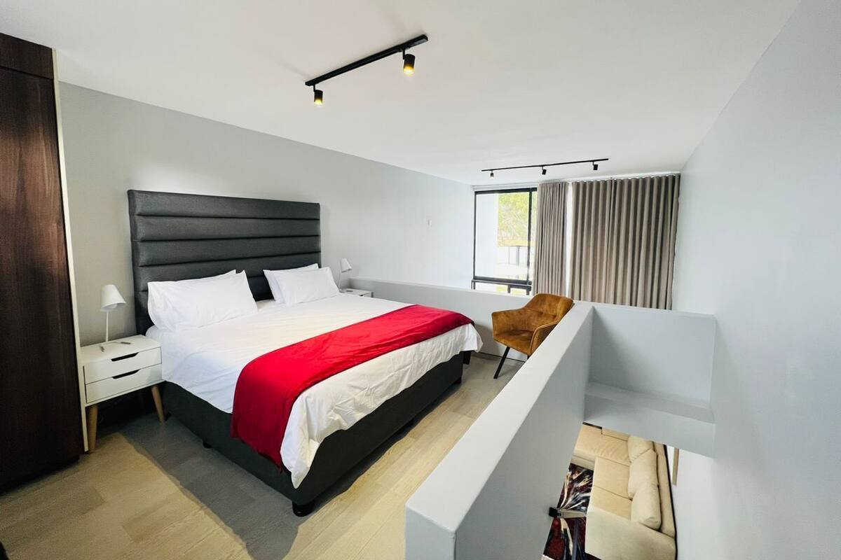 A modern bedroom with a large bed, a nightstand, a chair, and a window with curtains.