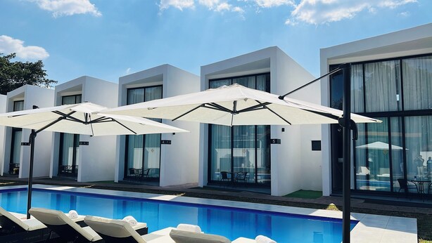 Un hotel moderno con piscina, sombrillas blancas y habitaciones numeradas.
