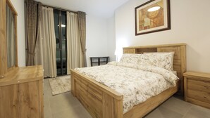 Une chambre à coucher avec un lit en bois, une table de chevet, une petite table, un miroir et une porte-fenêtre coulissante donnant sur un balcon.