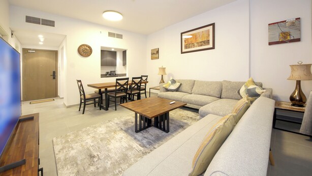 Un salon moderne comprenant un canapé, une table basse, une table à manger et des chaises. Il y a également un coin cuisine avec un évier et des placards.