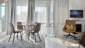 Ein modernes Wohnzimmer mit Essbereich, großen Fenstern und einem an der Wand montierten Flachbildfernseher.