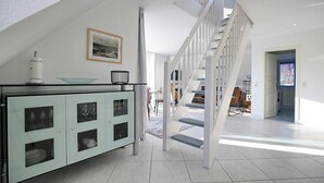 Eine moderne Küche mit Kochinsel aus Glas, weißen Schränken und einer Treppe, die zu einer oberen Ebene führt.
