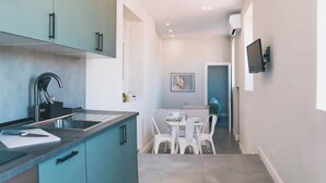A modern kitchen with a built-in stove, a sink, and a dining area with a table and chairs. - Apartment with panoramic terrace in historic center (Napoli)