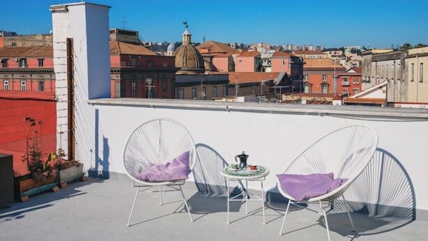 A rooftop terrace with two white wire-framed chairs and a small round table, overlooking a cityscape with historic buildings and a dome structure. - Apartment with panoramic terrace in historic center (Napoli)