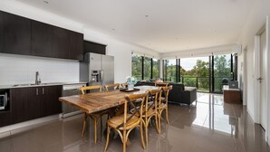 A modern kitchen with dark cabinetry, a wooden dining table, and a large window offering a view of greenery. - Beachfront Gem in Capel Sound (Capel Sound)