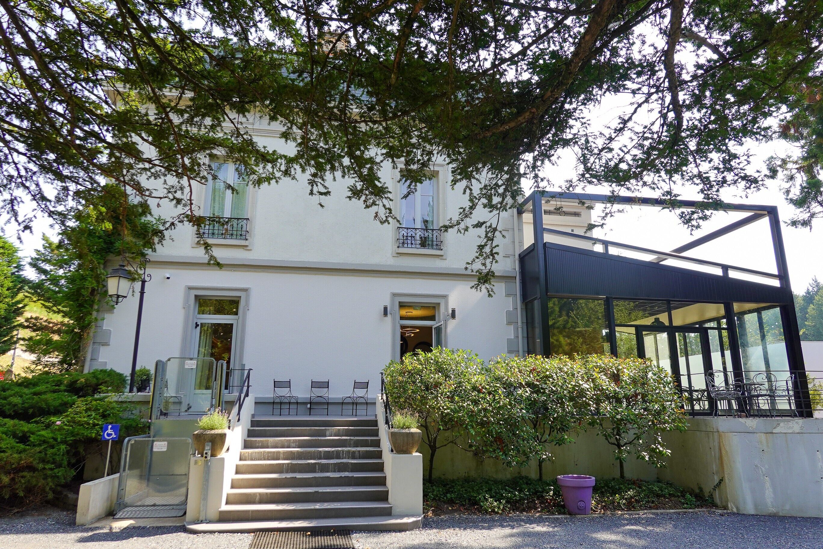 Un bâtiment doté d’un escalier menant à une porte, d’un espace extérieur abrité avec des sièges et d’une rampe d’accès pour les personnes à mobilité réduite.