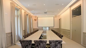 Ein Konferenzraum mit einem langen Tisch, gemusterten Stühlen, einer Projektionsleinwand und einem großen Fenster.