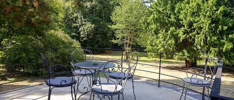 Une terrasse extérieure avec des chaises et une table en métal, entourée d’arbres.