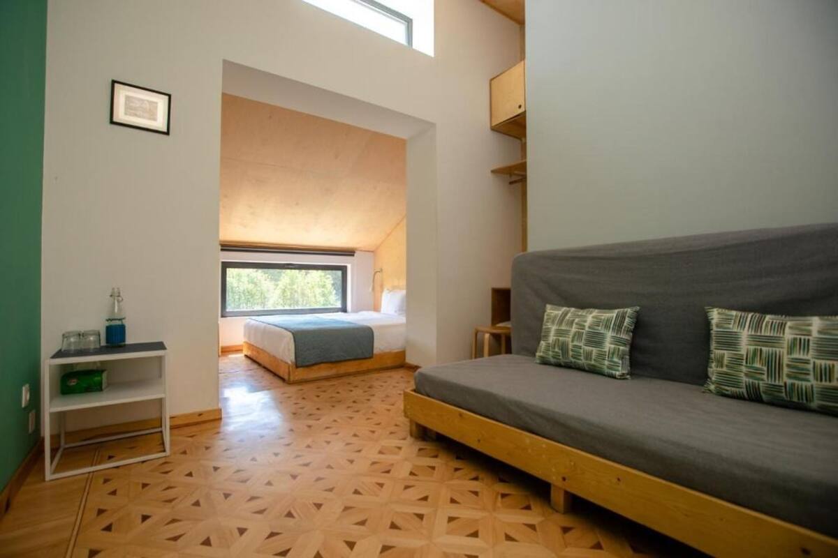 A room with a bed, a sofa, a shelf with items, and a window.