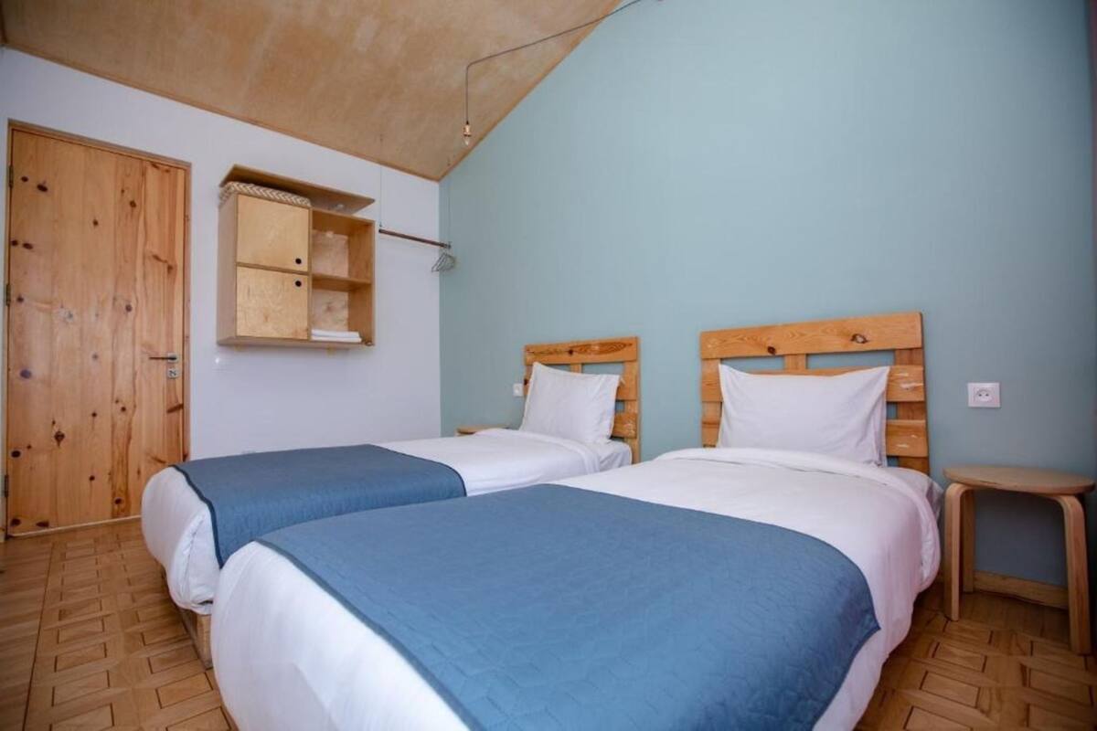 A room with two beds, wooden headboards, a small wooden stool, and a wooden wardrobe.