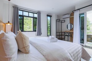 Ein Hotelzimmer mit einem großen Bett, einem Schreibtisch, einem Stuhl und einem Balkon mit Blick auf Grünflächen.