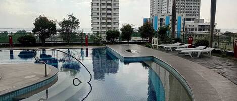 A swimming pool with a curved design, surrounded by lounge chairs and palm trees.