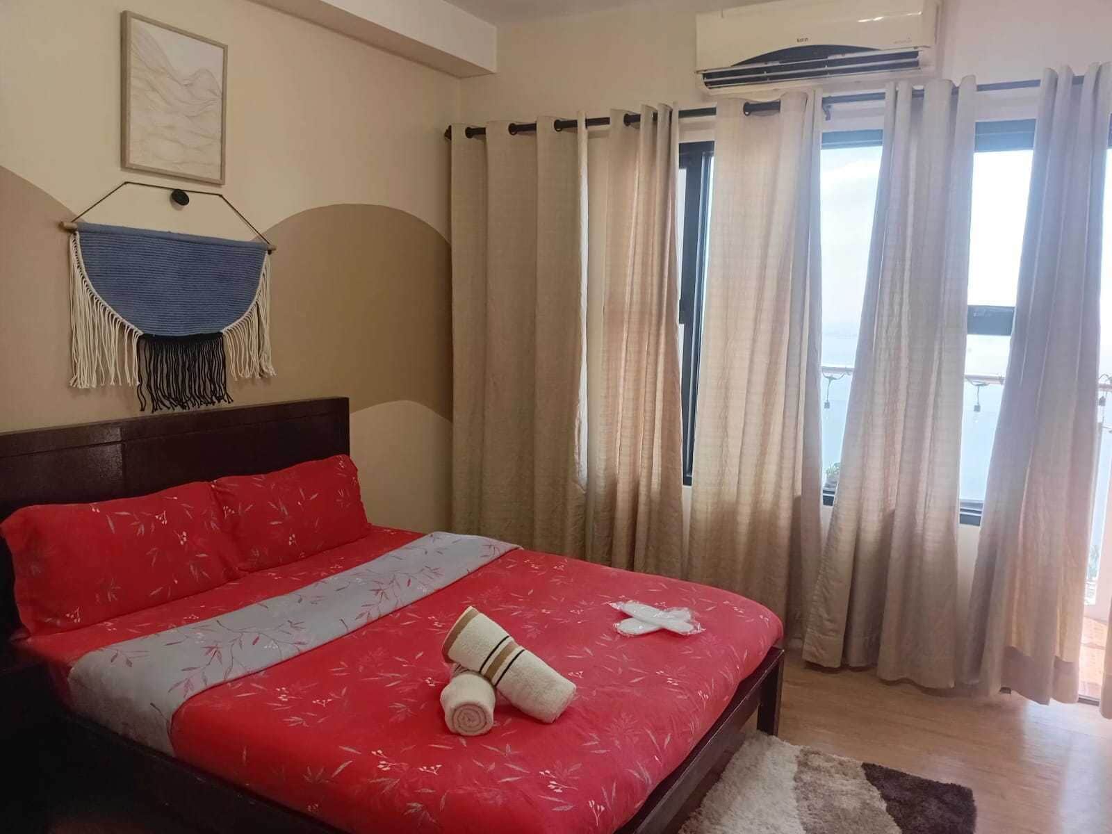 A hotel room with a bed, a wall-mounted macrame piece, and a window with curtains.