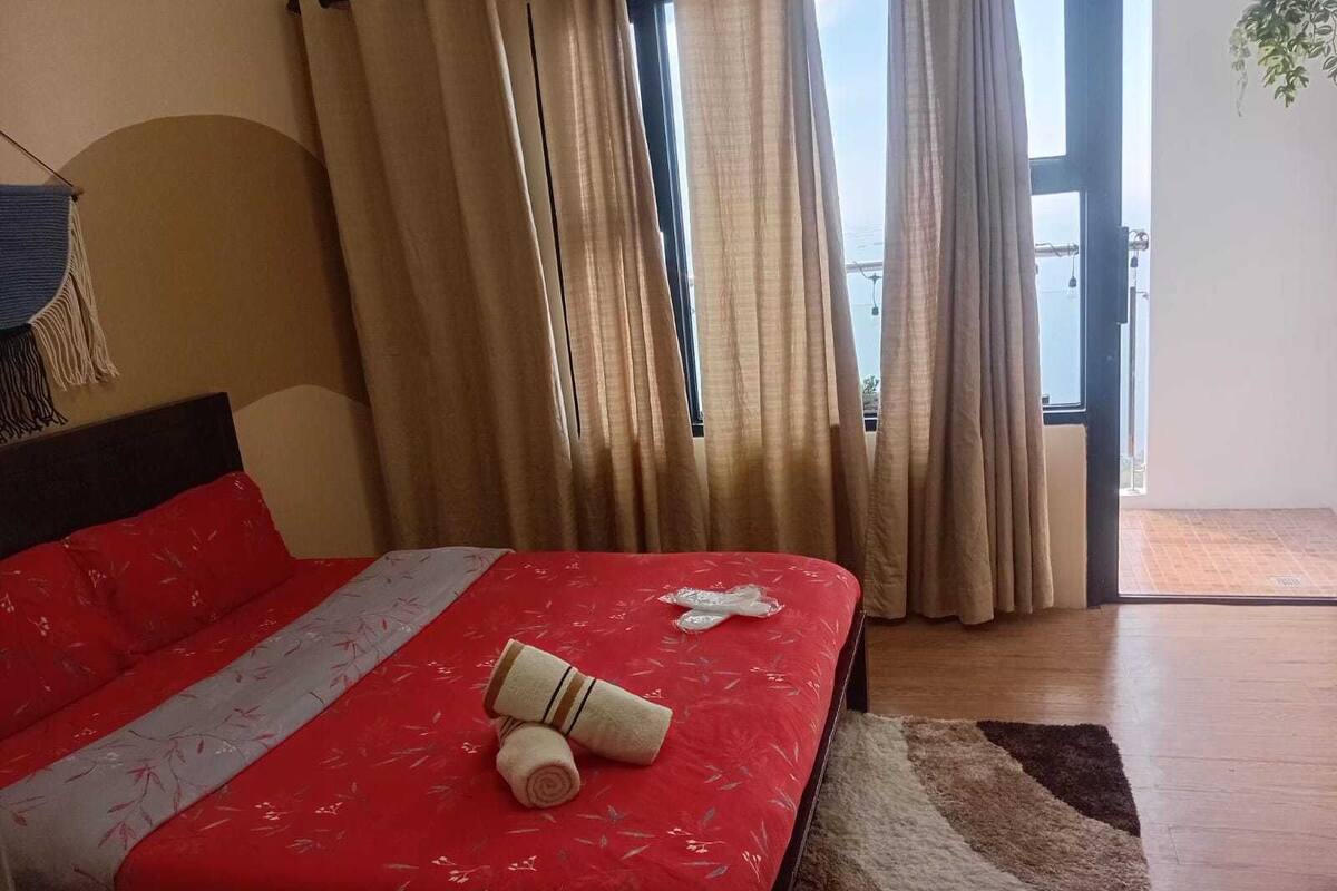 A hotel room with a large bed, beige curtains, and a view of the outdoors.