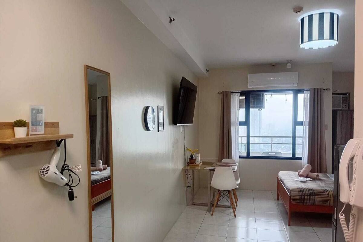 A hotel room with a bed, a chair, a desk, a mirror, a TV, and a window with a view.