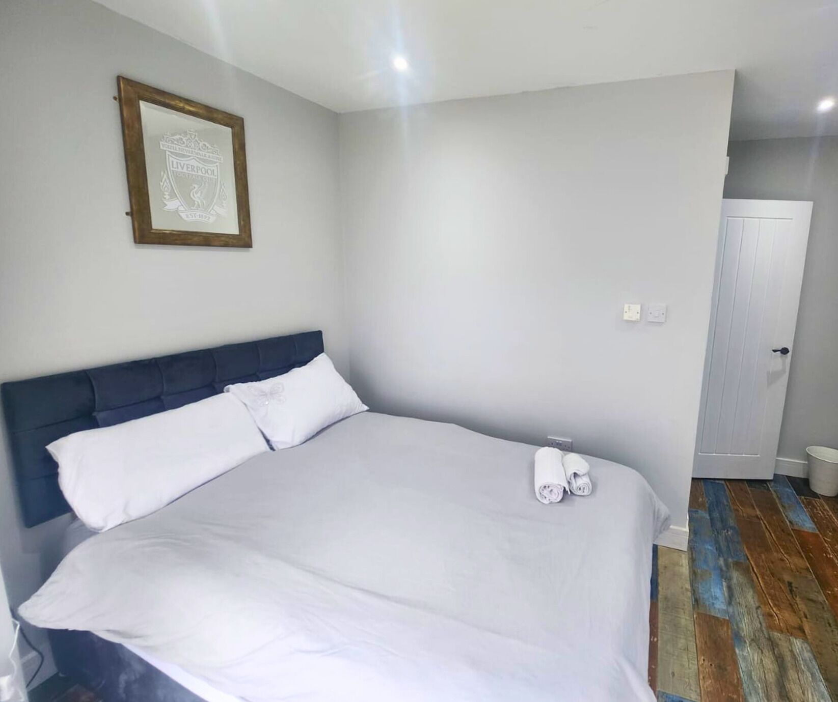 A bedroom with a large bed, a framed picture on the wall, and a door to the right.