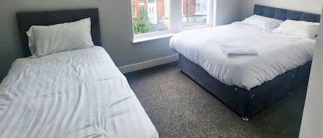 A hotel room with two single beds, a large window with a view of a red brick building, and a carpeted floor.