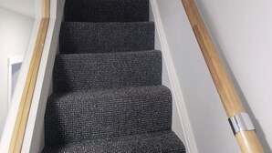 A staircase with dark patterned carpet and a wooden handrail. - The Red Lounge House - sleeps 14 (Liverpool)