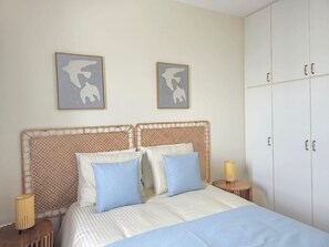 Une chambre à coucher comprenant un lit, deux œuvres d’art accrochées au mur, une armoire et une lampe de chevet.