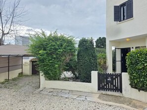 Un immeuble résidentiel avec une allée en gravier, un portail noir et un mur blanc.