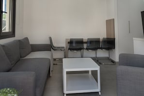 A modern living room with a grey sofa, a white coffee table, and a glass-top dining table with four chairs. - Seabreeze Residence by Staycom (Larnaca)