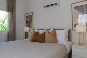 A neatly arranged hotel room with a bed, bedside lamps, a framed artwork, and an air conditioning unit. - Sienna Townhouse by Staycom (Paphos)