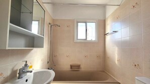 Une salle de bain avec une baignoire, un lavabo, un miroir et une fenêtre.