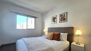 Une chambre d’hôtel avec un lit, deux lampes de chevet, une fenêtre et deux œuvres d’art accrochées au mur.