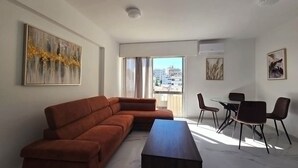 Un salon moderne avec un canapé d’angle, une table à manger en verre et des chaises, ainsi que des œuvres d’art accrochées aux murs.