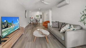 A modern living room with a flat-screen TV, a grey sofa, and a coffee table. - Alex Beach Stay | Pool, Gym, Beachfront walks (Sunshine Coast)