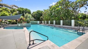 A swimming pool with a tiled deck, surrounded by palm trees and a fence. - Alex Beach Stay | Pool, Gym, Beachfront walks (Sunshine Coast)
