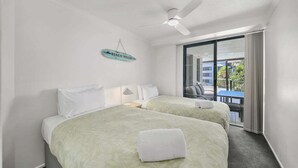 A hotel room with two beds, a ceiling fan, a balcony with a view, and a sign indicating it's a beach house. - Alex Beach Stay | Pool, Gym, Beachfront walks (Sunshine Coast)