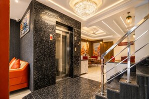 A hotel lobby with a marble reception desk, a modern elevator, a staircase, and a dining area with red chairs. - Hotel Euronite Suites by RARO Hospitality Near IGI Airport Delhi (New Delhi)