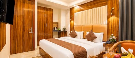 Una habitación de hotel con una cama grande, paneles de madera, un televisor de pantalla plana, una pequeña kitchenette y un frutero en la mesita de noche.
