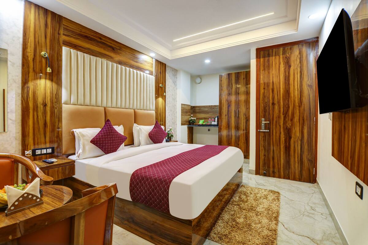 Habitación de hotel con una cama grande, paneles de madera, televisión, escritorio con silla y una pequeña kitchenette.