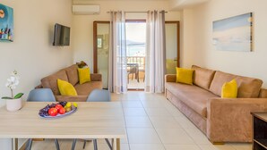 Een moderne woonkamer met een bank, een eettafel met fruit en uitzicht op een balkon.