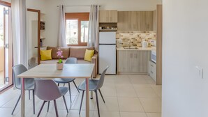 Een moderne keuken met een koelkast, spoelbak en houten kastjes. Er is een eethoek met een tafel en stoelen, plus een bank met kussens.