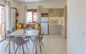 A modern kitchen with a refrigerator, sink, and wooden cabinets. There is a dining area with a table and chairs, and a sofa with cushions. - Aloustina Apartment for 4, 50m from the Sea in Archangelos (Archangelos)