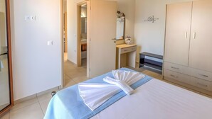 Een slaapkamer met een bed, een kledingkast, een zichtbare badkamer door een geopende deur en een nachtkastje met een lamp.