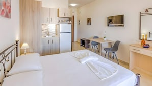 Ein Hotelzimmer mit Bett, Schreibtisch, Stuhl, einer kleinen Küchenzeile und einem Fernseher.