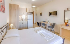 A hotel room with a bed, a desk, a chair, a small kitchenette, and a TV. - Aloustina Apartment 50m from the Sea in Archangelos (Archangelos)