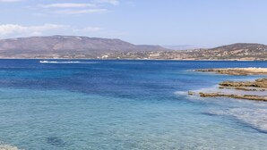 Eine Küstenlandschaft mit klarem, blauem Wasser, felsigen Ufern und Bergen im Hintergrund.