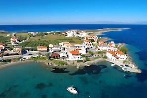 An aerial view of a coastal village with houses, clear blue waters, and a boat docked near the shore. - Aloustina Apartment 50m from the Sea in Archangelos (Archangelos)