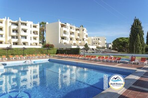 A swimming pool with lounge chairs, a clear blue sky, and a multi-story building with balconies. - Jardim Cozy Apartment With Pools Near the Old Town (Albufeira)