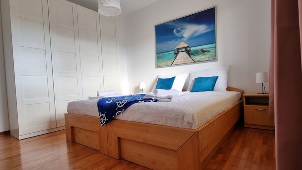 Ein Schlafzimmer mit einem hölzernen Bett, einem weißen Kleiderschrank und einem Gemälde, das eine Strandansicht zeigt.